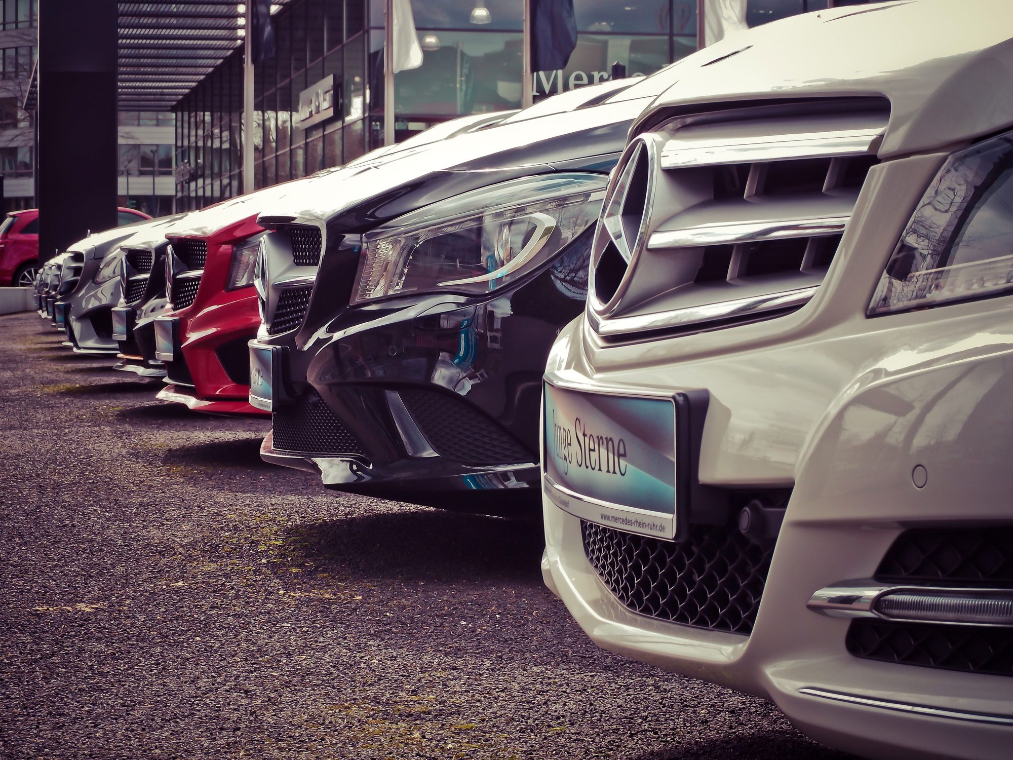 Vehicles parked in a row outside a dealership building.