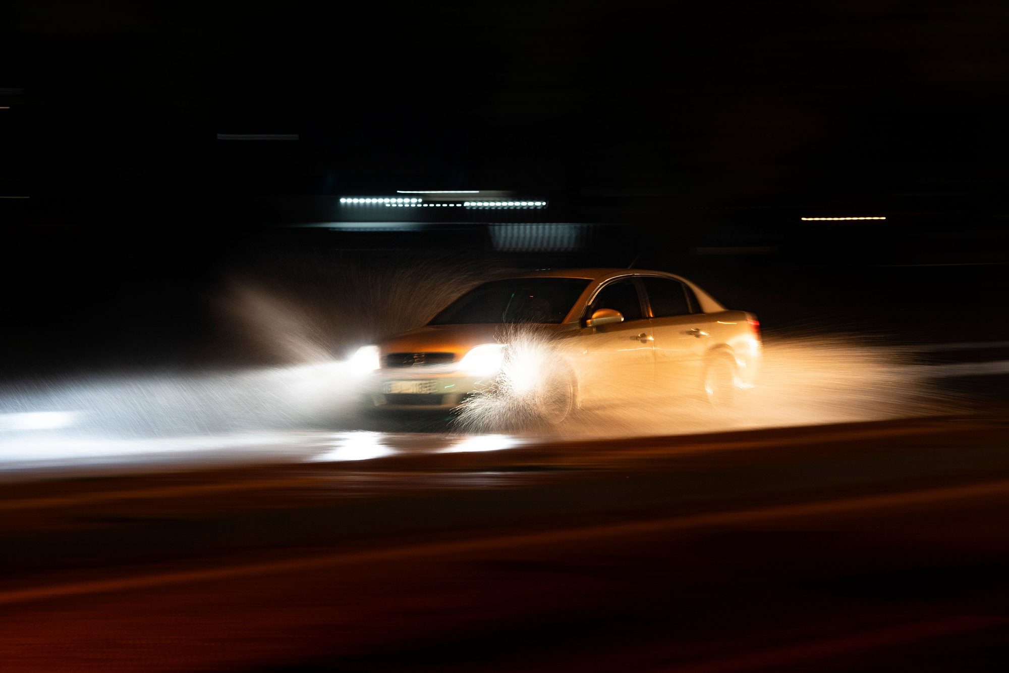 A vehicle driving through rain at night, headlights blazing through the spray.